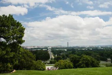 A summertime view of Washington, D.C., from Arlington National Cemetery includes green grass and a healthy tree canopy.