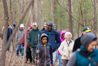 More than a dozen hikers walk along a wooded trail in Cumberland County, Pennsylvania, as part of an early spring hike hosted by the Nature Conservancy.